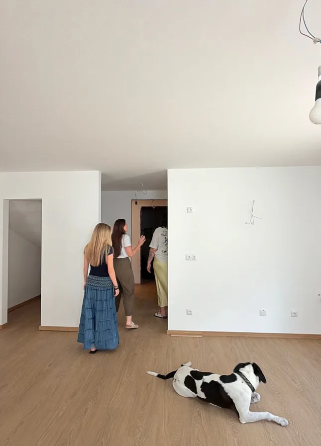 Three colleagues walking through an empty apartment while the studio dog lies on the wooden floor