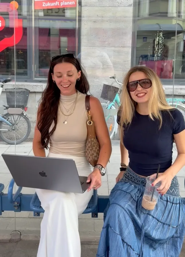 Two colleagues sharing a laptop on a bench outside