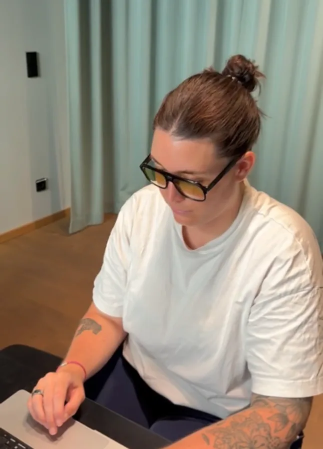 Working at a laptop in glasses in front of a curtained window