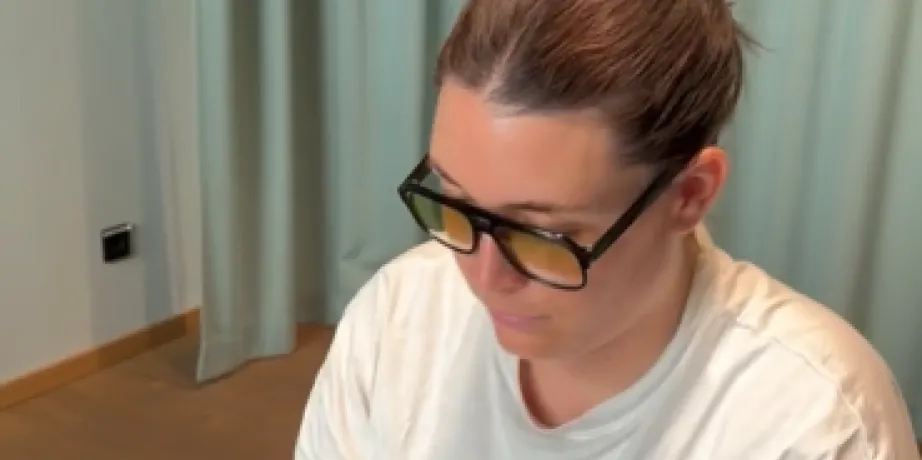 Working at a laptop in glasses in front of a curtained window
